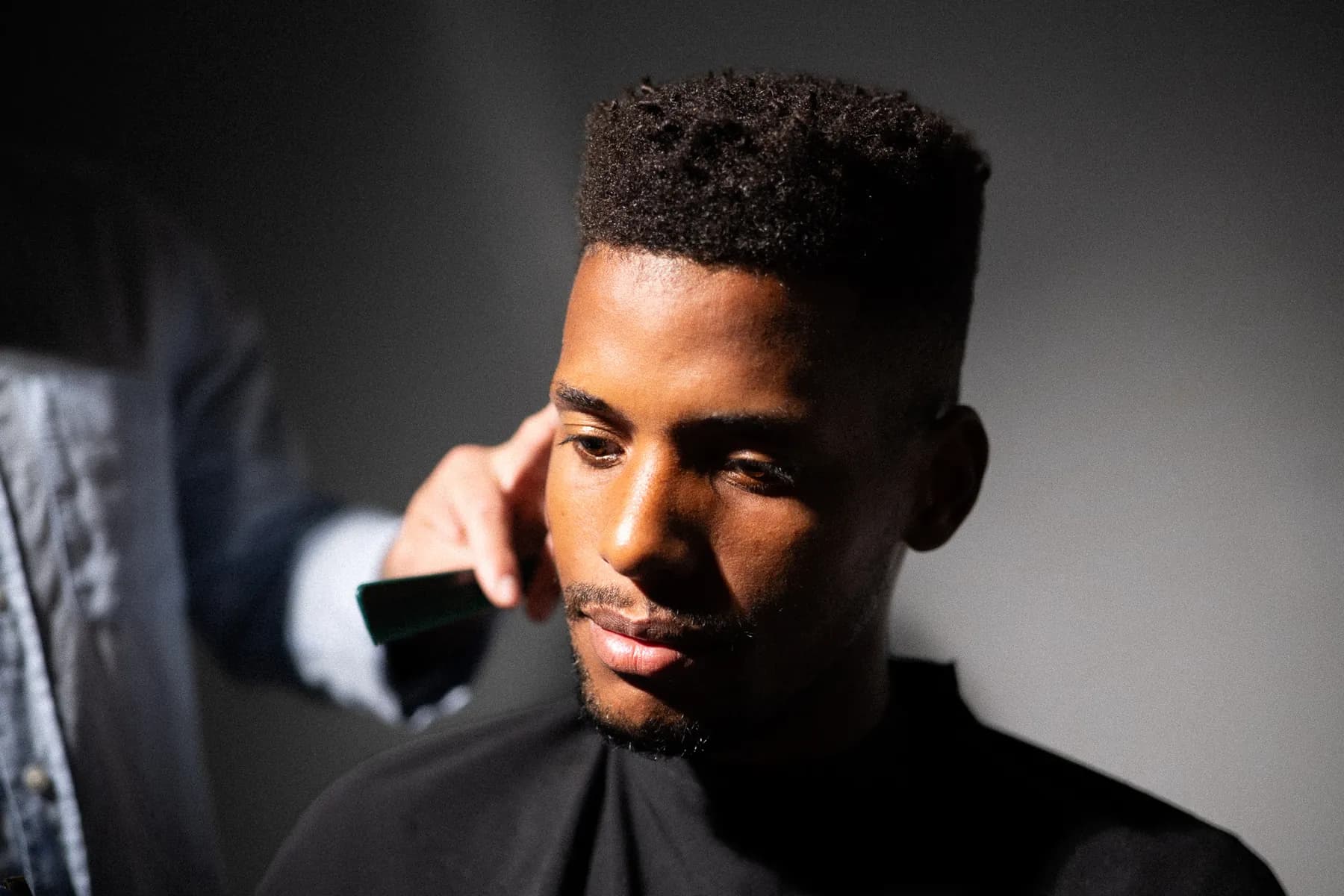 Cliente con la capa puesta mientras el barbero estudia su corte
